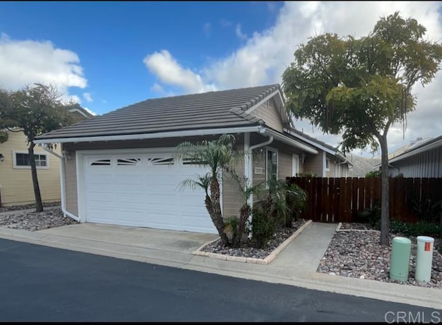 view of property exterior with an attached garage, fence, concrete driveway, and a tiled roof