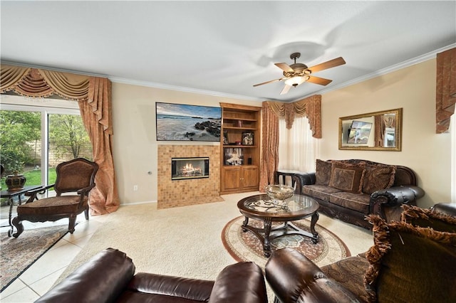 living area featuring ceiling fan, a tile fireplace, baseboards, tile patterned floors, and crown molding