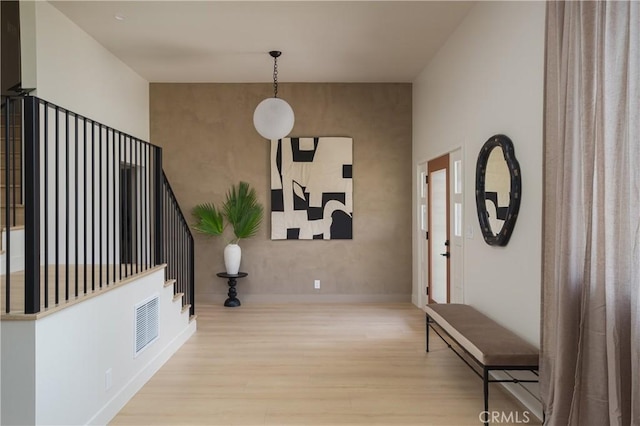 foyer with an accent wall, visible vents, baseboards, and wood finished floors