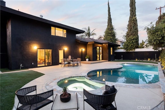 pool at dusk featuring a patio area, a pool with connected hot tub, fence, and a yard