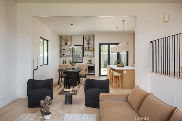 living area with beverage cooler, light wood finished floors, baseboards, and a healthy amount of sunlight