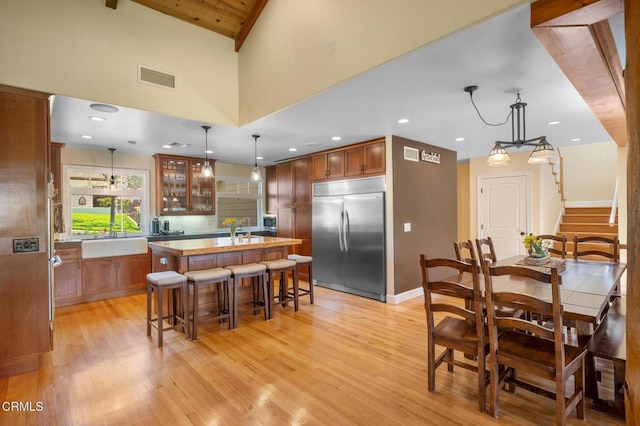 kitchen featuring built in fridge, a breakfast bar, a kitchen island, visible vents, and glass insert cabinets