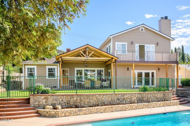 rear view of house with a ceiling fan, fence private yard, a chimney, and a balcony