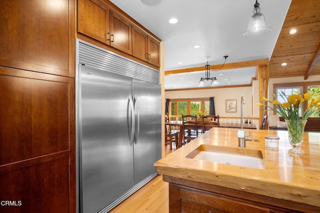 kitchen featuring built in refrigerator, a sink, brown cabinetry, and pendant lighting