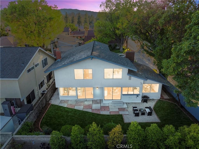 back of house at dusk with stucco siding, a patio, and a fenced backyard