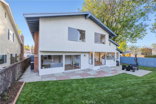 back of house featuring a fenced backyard, a lawn, a patio, and stucco siding