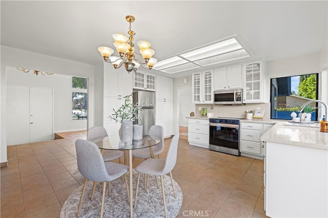 kitchen featuring backsplash, stainless steel appliances, a notable chandelier, white cabinetry, and a sink