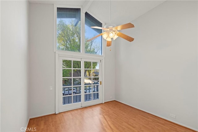 spare room with baseboards, high vaulted ceiling, a ceiling fan, and wood finished floors