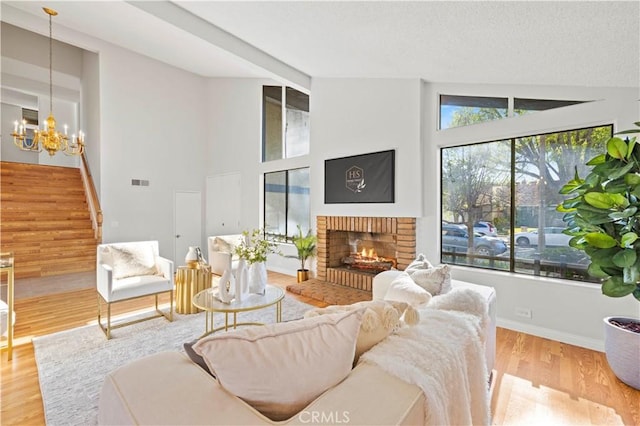 living area with wood finished floors, visible vents, stairs, a brick fireplace, and a chandelier