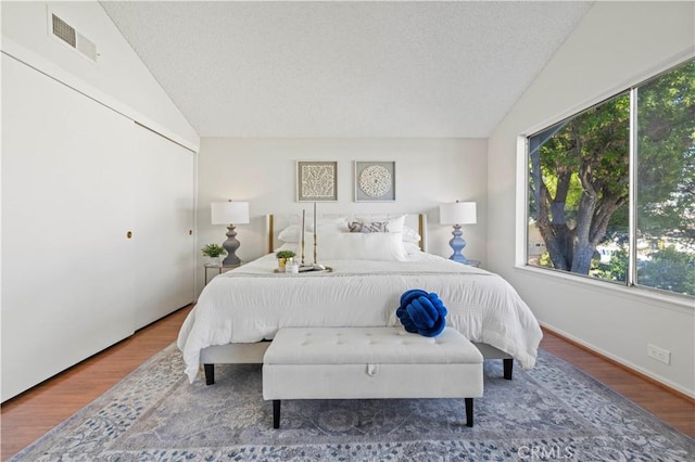 bedroom with visible vents, a textured ceiling, wood finished floors, and vaulted ceiling