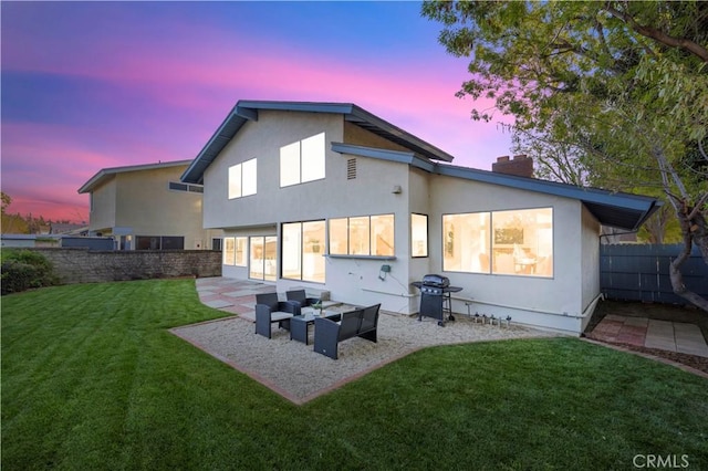 back of property at dusk with stucco siding, a lawn, a patio, fence, and a chimney