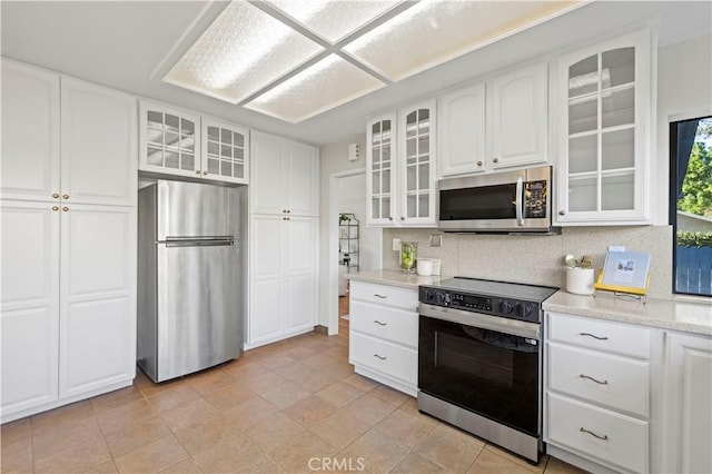 kitchen featuring decorative backsplash, appliances with stainless steel finishes, white cabinets, glass insert cabinets, and light stone countertops