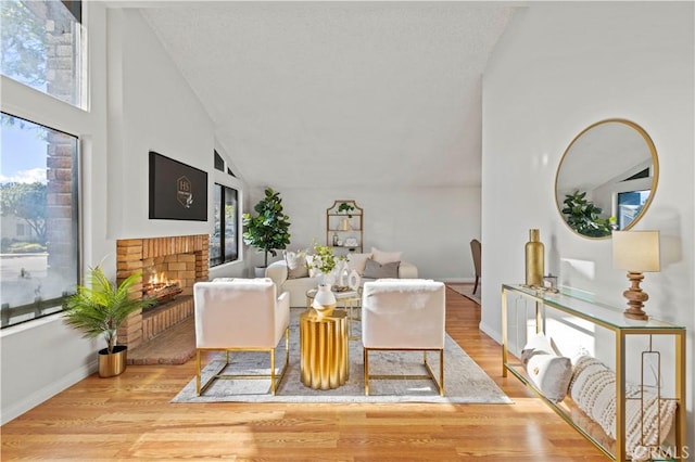 living area with a brick fireplace, wood finished floors, baseboards, and high vaulted ceiling