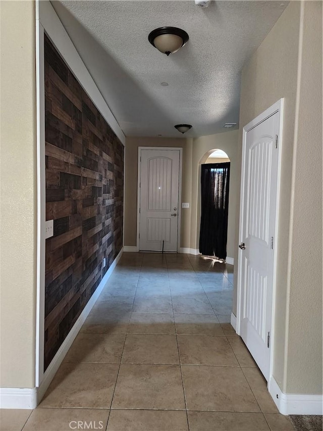 corridor featuring light tile patterned floors, baseboards, arched walkways, and a textured ceiling