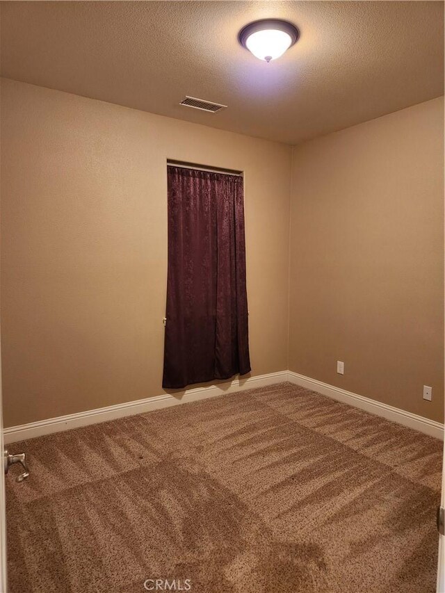 empty room featuring carpet floors, visible vents, a textured ceiling, and baseboards