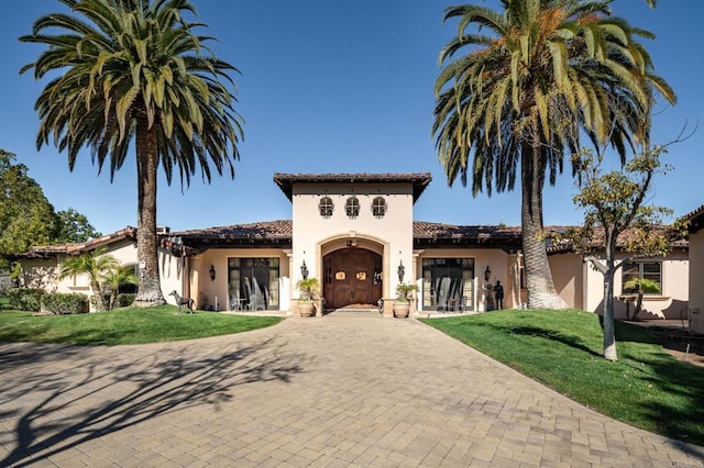 mediterranean / spanish-style home featuring a garage, decorative driveway, a front lawn, and stucco siding