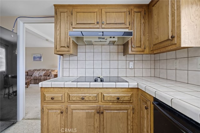 kitchen featuring tile counters, decorative backsplash, brown cabinetry, under cabinet range hood, and black appliances