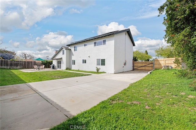 rear view of house with solar panels, stucco siding, a lawn, a patio area, and a fenced backyard