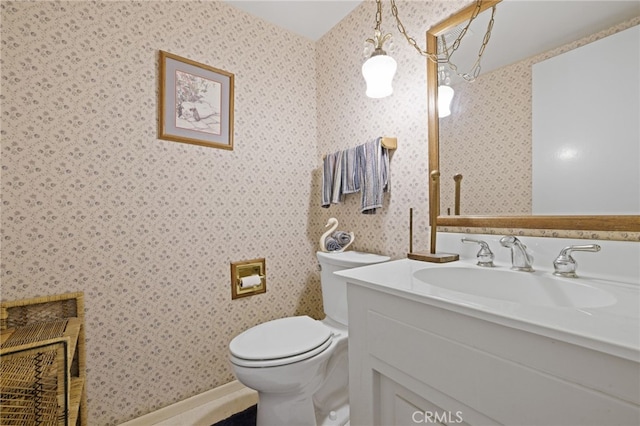 half bathroom featuring toilet, wallpapered walls, and vanity