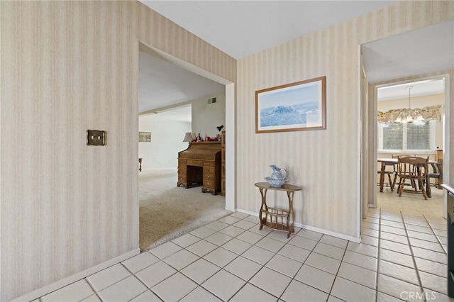 hallway with light tile patterned floors, a notable chandelier, light colored carpet, baseboards, and wallpapered walls