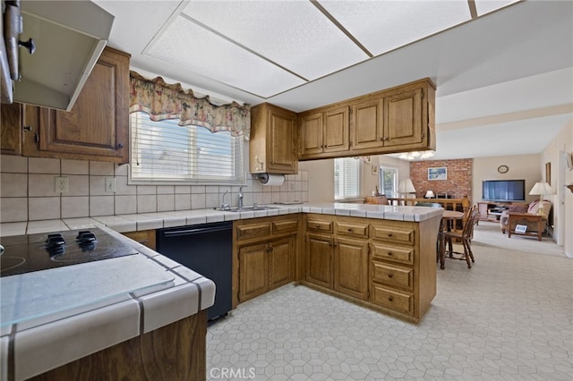 kitchen featuring a peninsula, a sink, open floor plan, black appliances, and brown cabinetry