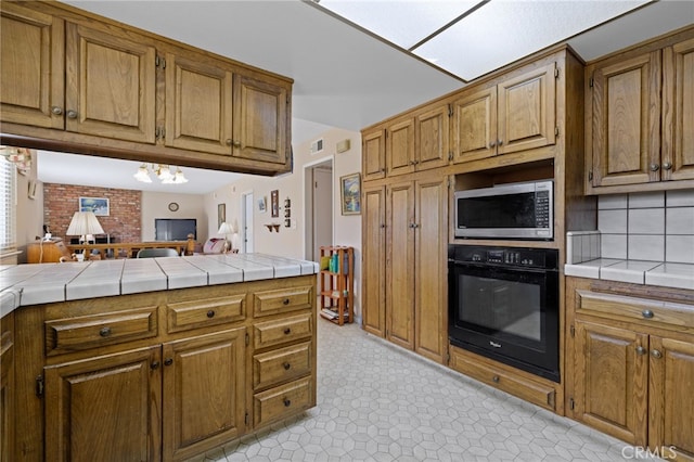 kitchen featuring tile countertops, stainless steel microwave, brown cabinetry, and black oven