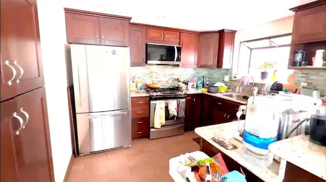 kitchen featuring appliances with stainless steel finishes, a sink, light stone countertops, and tasteful backsplash