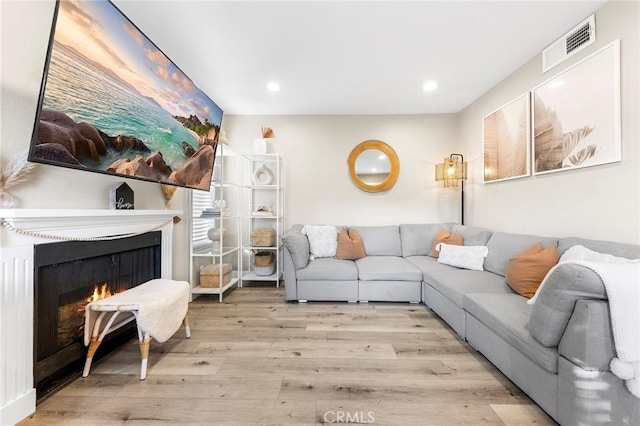 living area with recessed lighting, a warm lit fireplace, visible vents, and wood finished floors