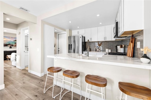 kitchen featuring light wood finished floors, tasteful backsplash, a peninsula, stainless steel refrigerator with ice dispenser, and a sink