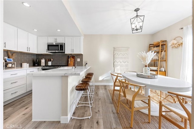 kitchen with light countertops, stainless steel microwave, decorative backsplash, light wood-type flooring, and a kitchen bar