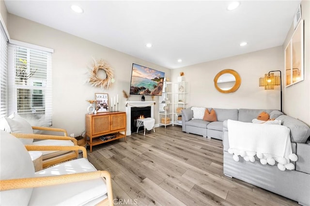 living room featuring a warm lit fireplace, light wood-type flooring, visible vents, and recessed lighting