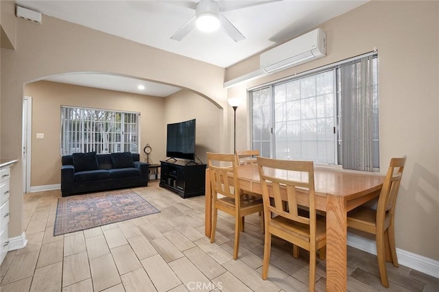 dining space with baseboards, arched walkways, ceiling fan, an AC wall unit, and light wood-type flooring