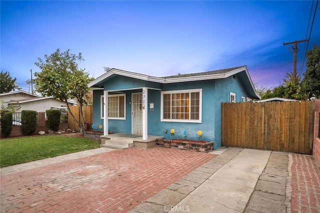 bungalow-style house with a porch, fence, a front lawn, and stucco siding