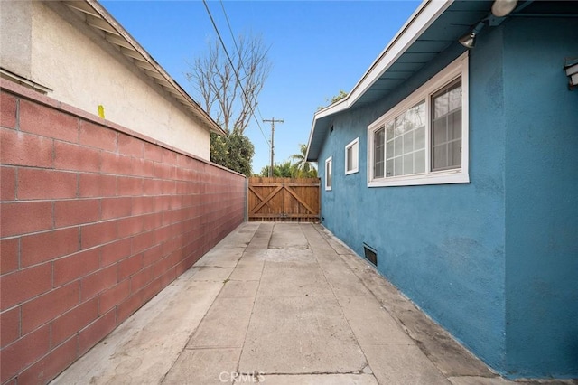 view of side of property featuring a gate, fence, and stucco siding