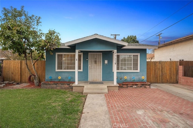 bungalow-style home featuring a front yard, fence, and stucco siding