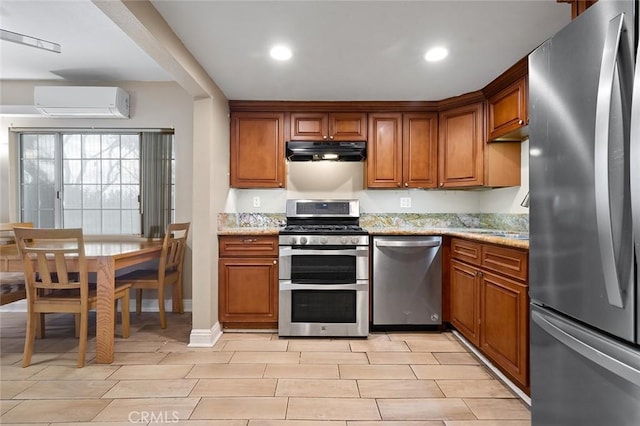 kitchen featuring appliances with stainless steel finishes, an AC wall unit, brown cabinets, and under cabinet range hood