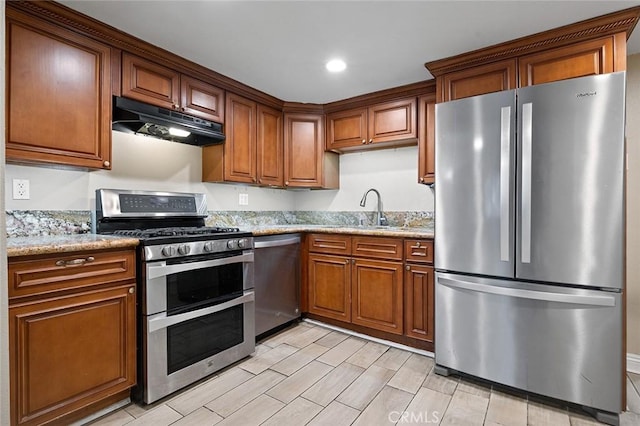 kitchen with a sink, appliances with stainless steel finishes, brown cabinets, and under cabinet range hood