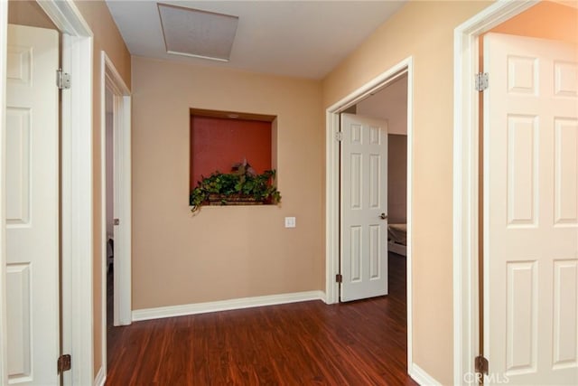 corridor with attic access, dark wood-style flooring, and baseboards