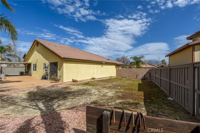 view of side of home featuring stucco siding, a tiled roof, a fenced backyard, and a patio