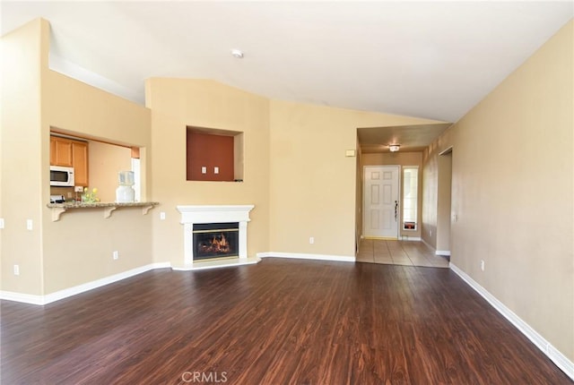 unfurnished living room featuring dark wood-style floors, baseboards, vaulted ceiling, and a glass covered fireplace