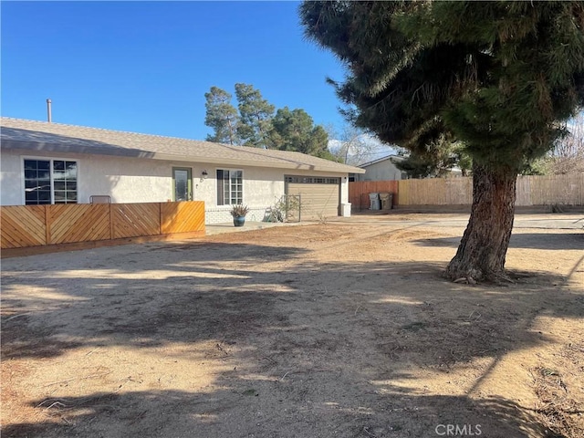 back of property featuring a garage, driveway, fence, and stucco siding