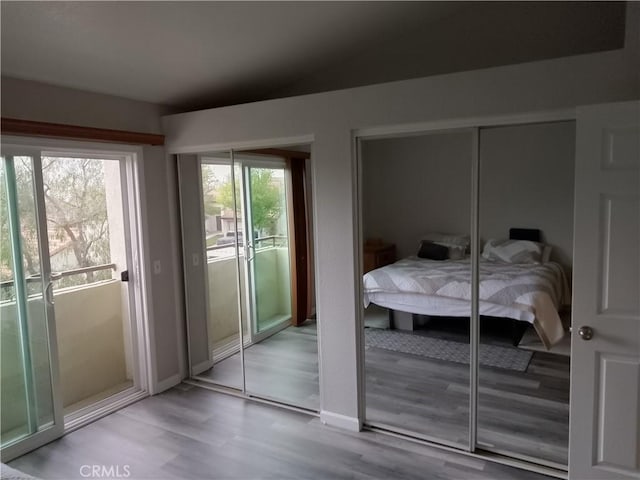 bedroom featuring access to exterior, baseboards, light wood finished floors, and two closets