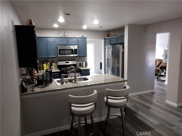 kitchen with light stone counters, appliances with stainless steel finishes, a sink, blue cabinets, and a peninsula