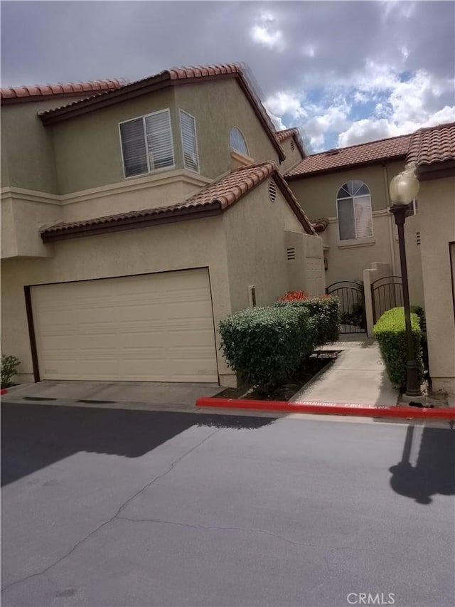 view of front of house featuring a garage, driveway, a tile roof, a gate, and stucco siding