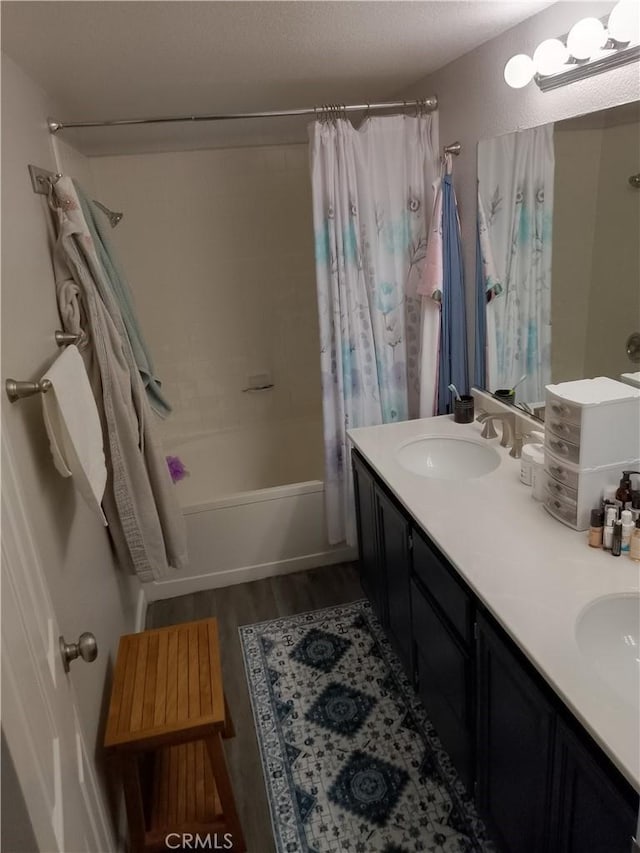 full bathroom featuring double vanity, wood finished floors, a sink, and shower / bathtub combination with curtain