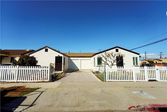 view of front of property featuring driveway, a fenced front yard, an attached garage, and stucco siding