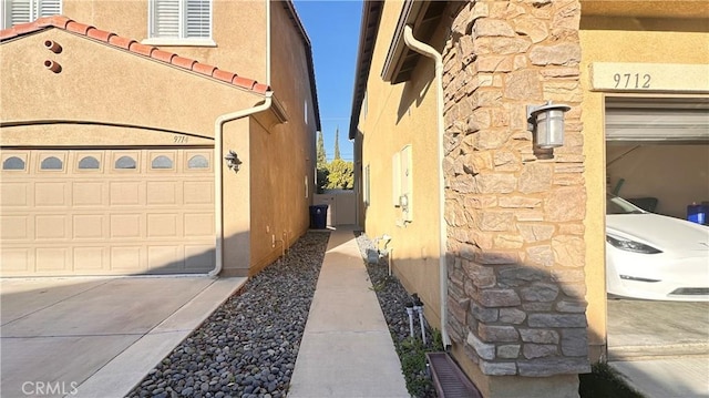 view of property exterior featuring a tile roof, stucco siding, concrete driveway, an attached garage, and stone siding