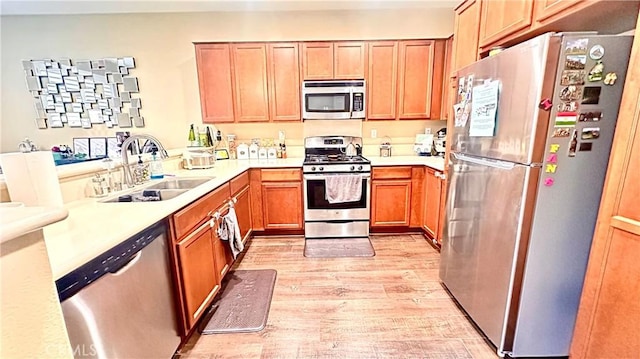 kitchen featuring stainless steel appliances, light wood finished floors, a sink, and light countertops