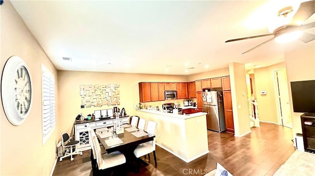 kitchen with a ceiling fan, appliances with stainless steel finishes, dark wood-style flooring, a peninsula, and light countertops