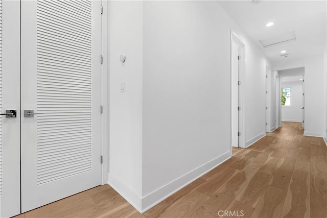 corridor featuring attic access, baseboards, and light wood finished floors